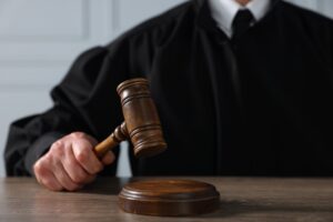 Judge in black robe holding a wooden gavel over a sound block, symbolizing legal authority, court decisions, and justice system proceedings.