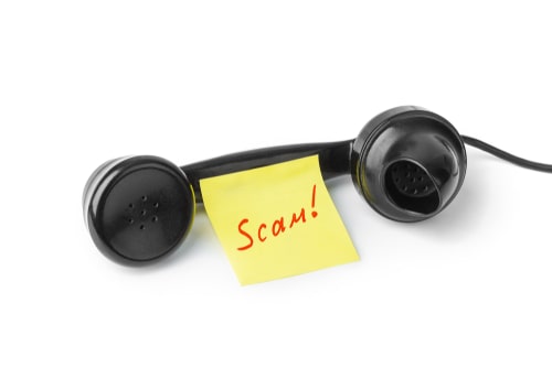 Black telephone receiver with a yellow sticky note labeled "Scam!" attached to it