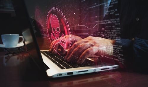 Person typing on a laptop with a red skull warning symbol representing a cyber threat