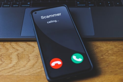 Smartphone screen showing an incoming call labeled "Scammer" placed on a laptop keyboard
