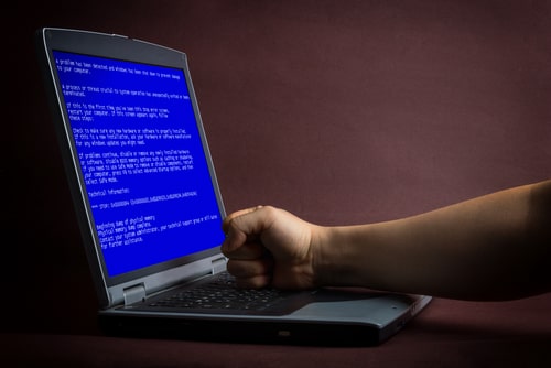 Person punching a laptop displaying the blue screen of death (BSOD) out of frustration