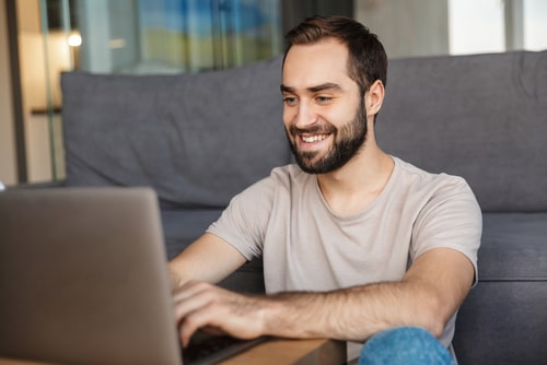 Smiling man using a laptop at home, representing learning or mastering basic computer skills