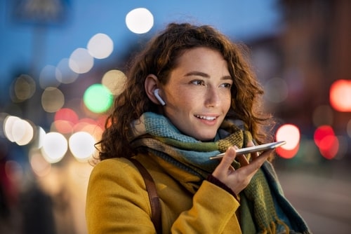 Woman using voice assistant like Siri on smartphone while walking outdoors