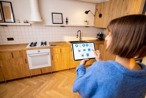 Woman using tablet to control smart home appliances in modern kitchen