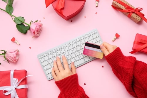 Hands holding credit card and typing on keyboard for online shopping, surrounded by Valentine's Day gifts and roses