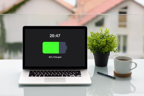 Laptop on desk showing 82% battery charged with time display and office items around