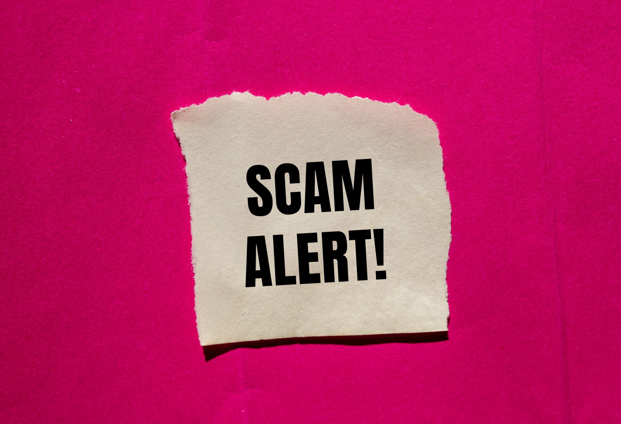 Torn paper with bold text Scam Alert on pink background, warning about fraud or deception