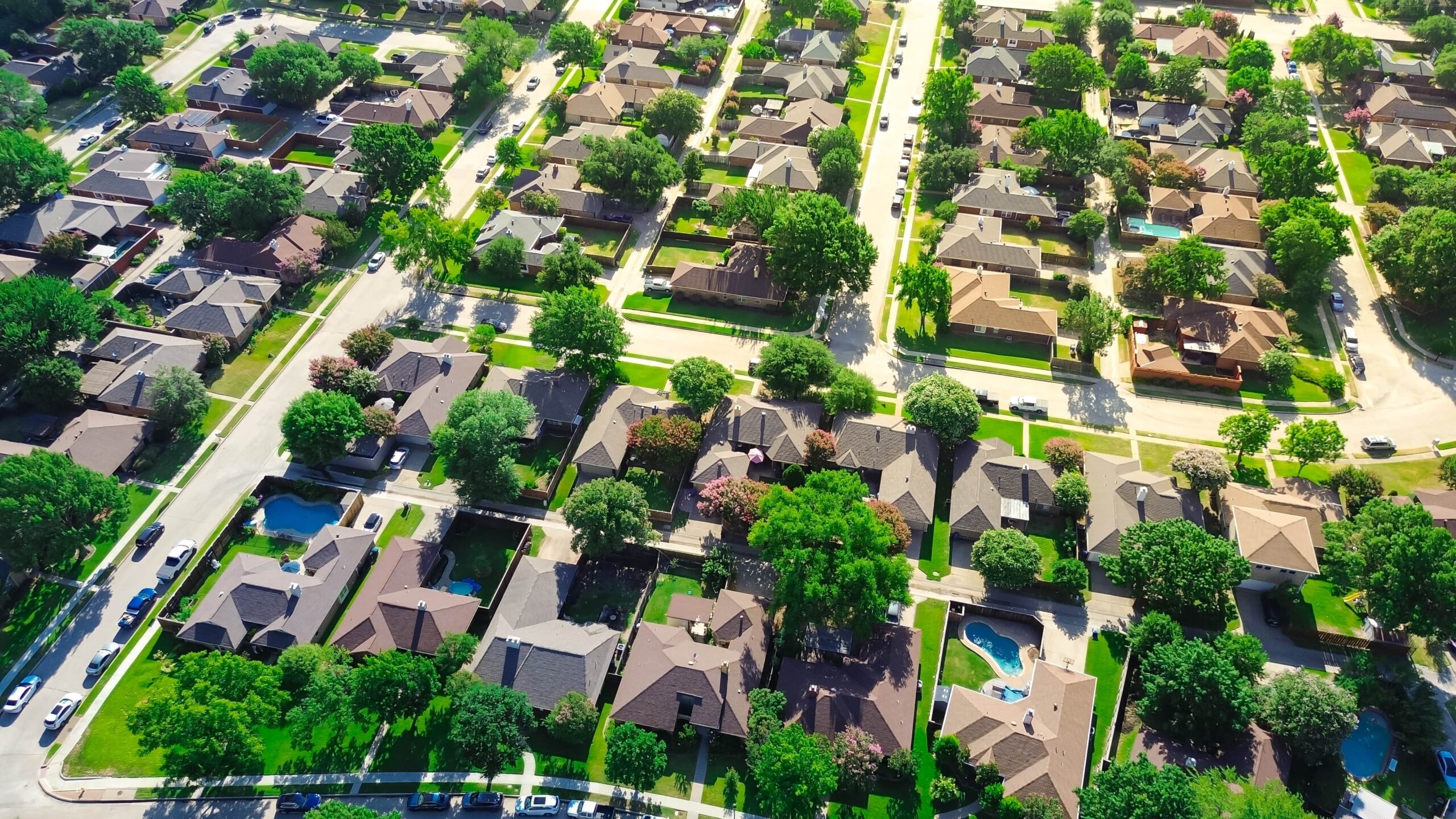 Aerial view of suburban residential neighborhood with houses, streets, trees, and swimming pools