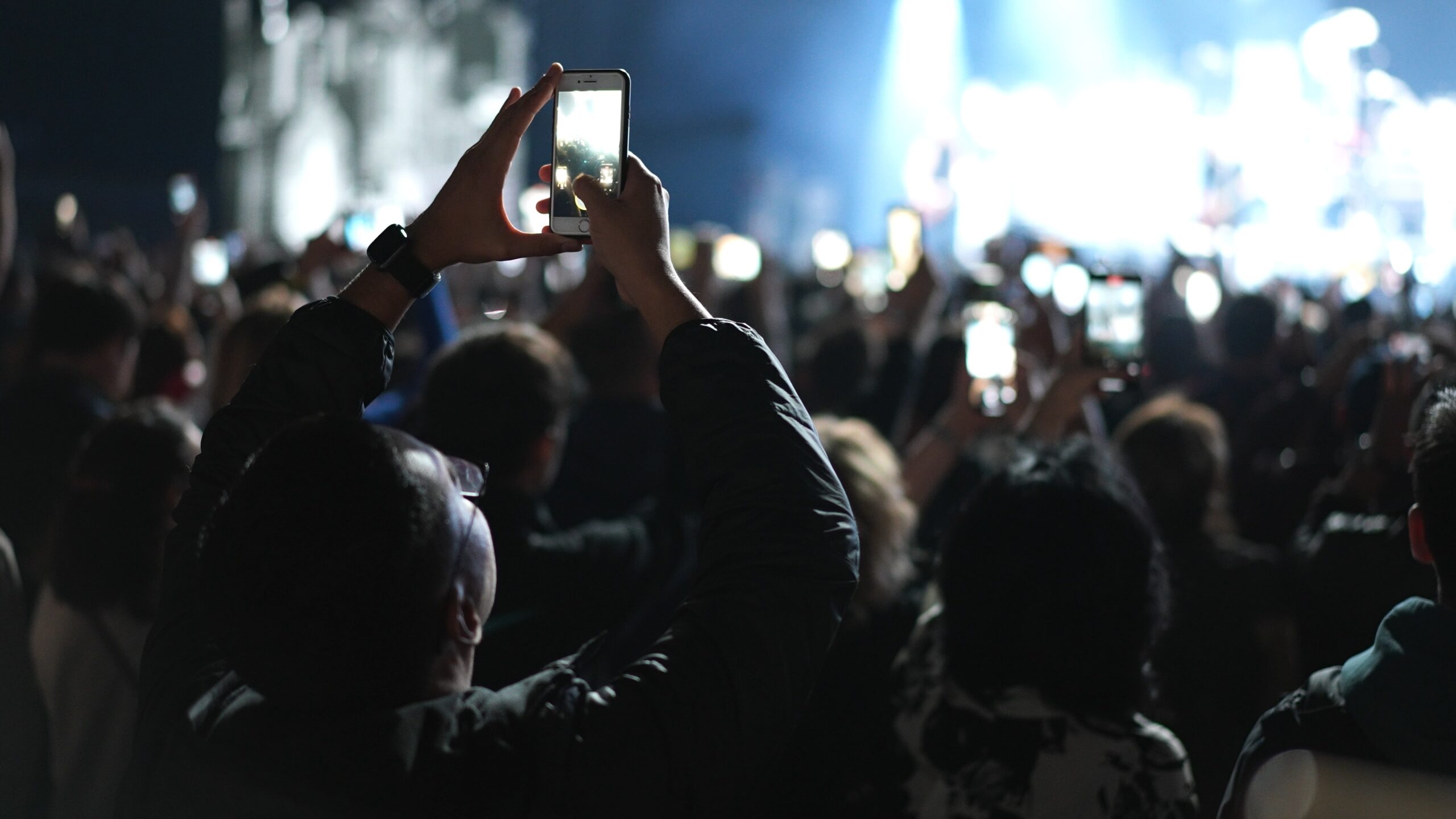 Crowd recording a live concert with smartphones, person in foreground holding up an phone