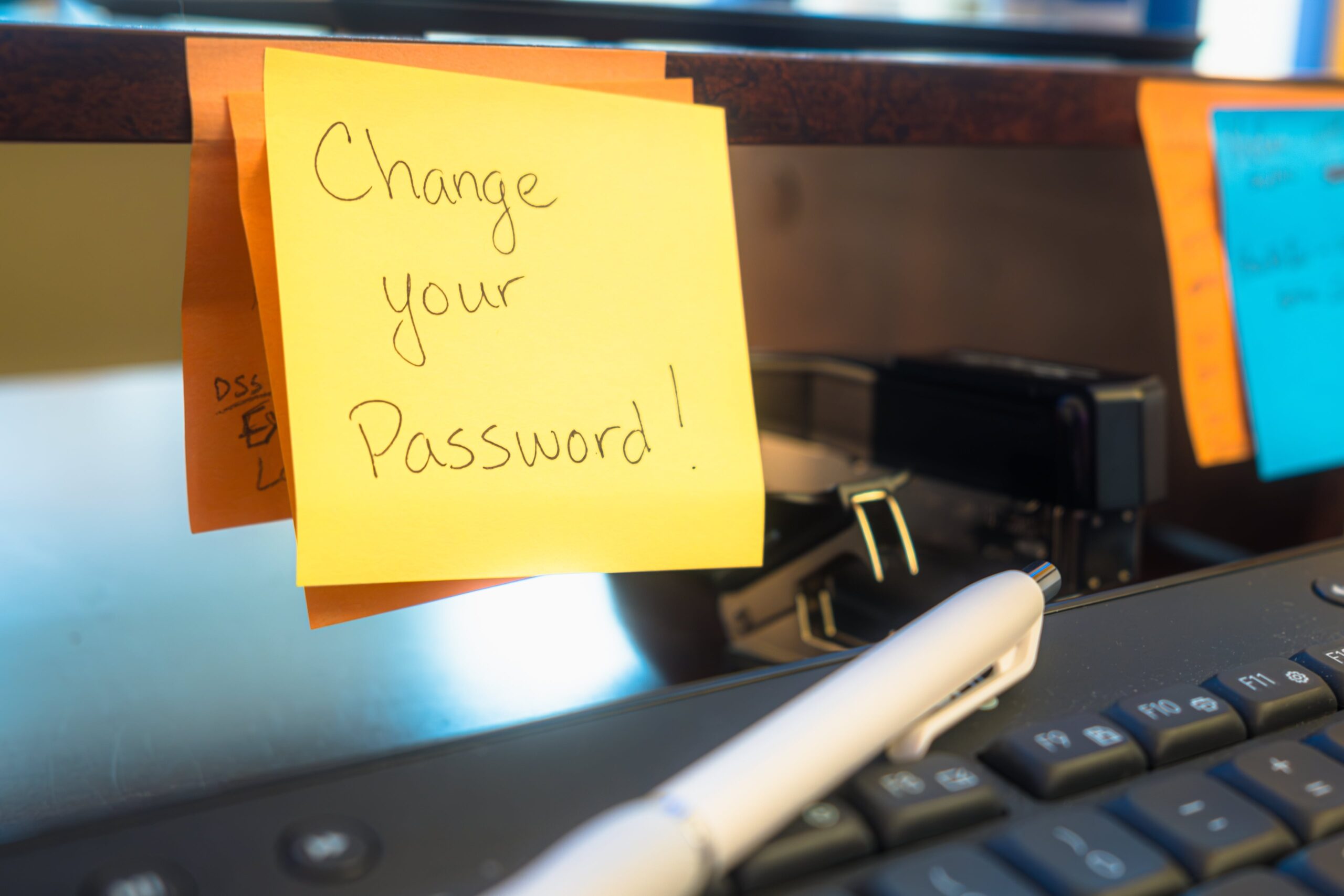 Sticky note with message 'Change your Password!' on office desk above keyboard