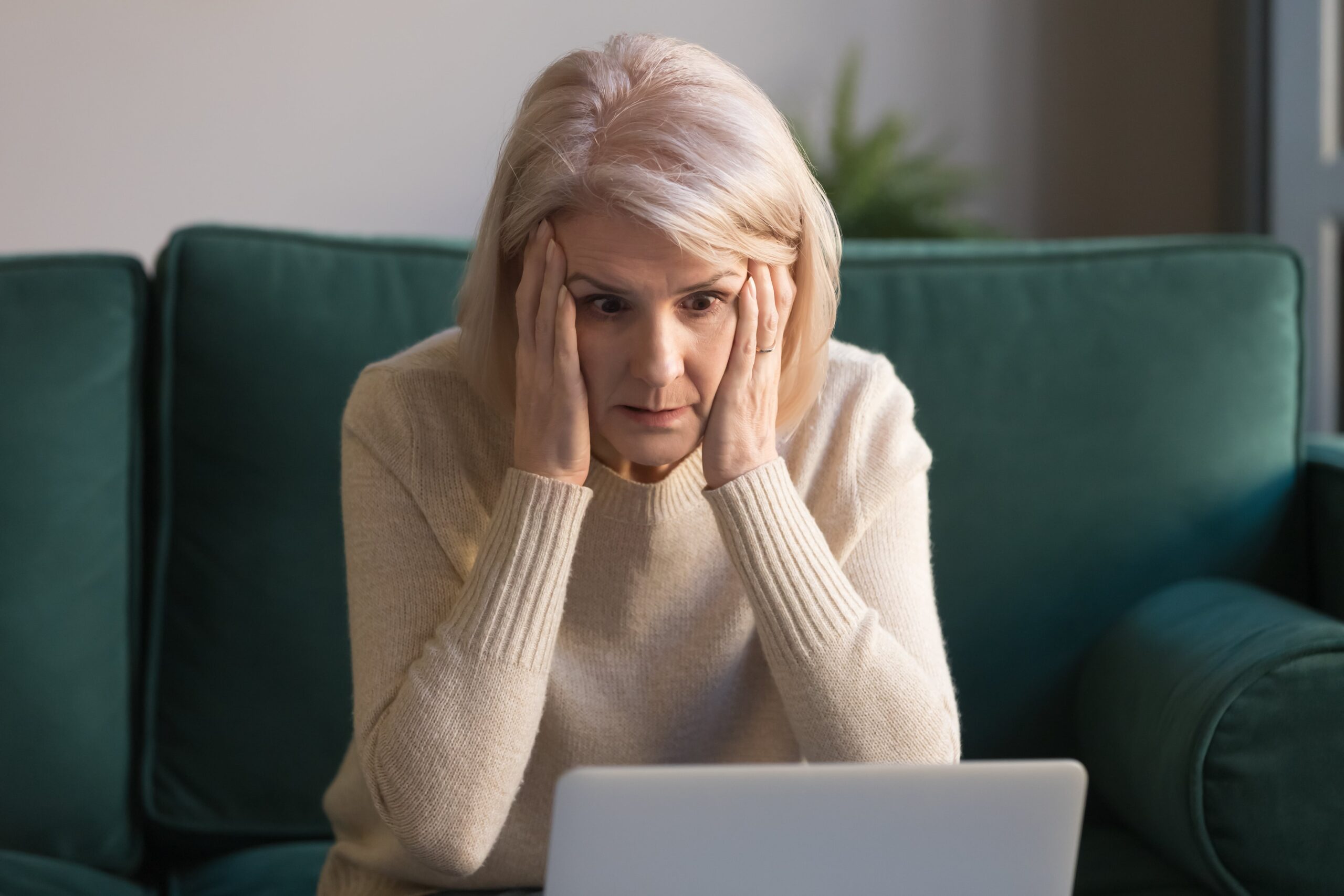Older woman sitting on green couch looking frustrated at her frozen computer