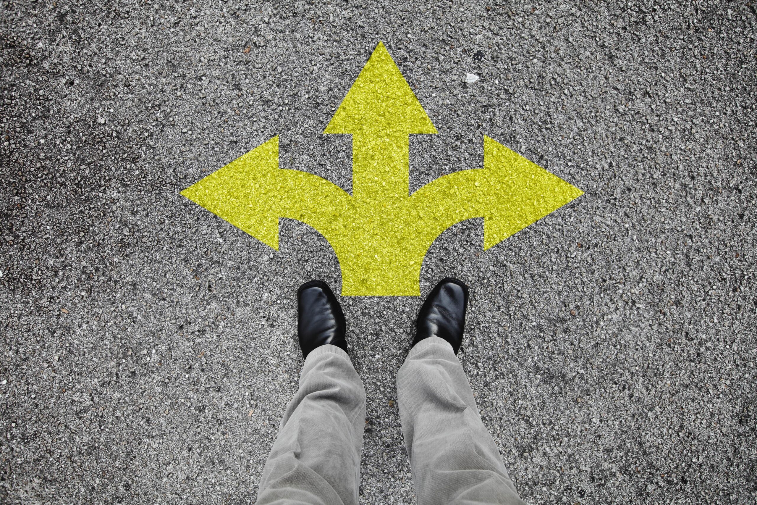 person standing on pavement with 3 yellow arrows pointing opposite directions, having to make a choice