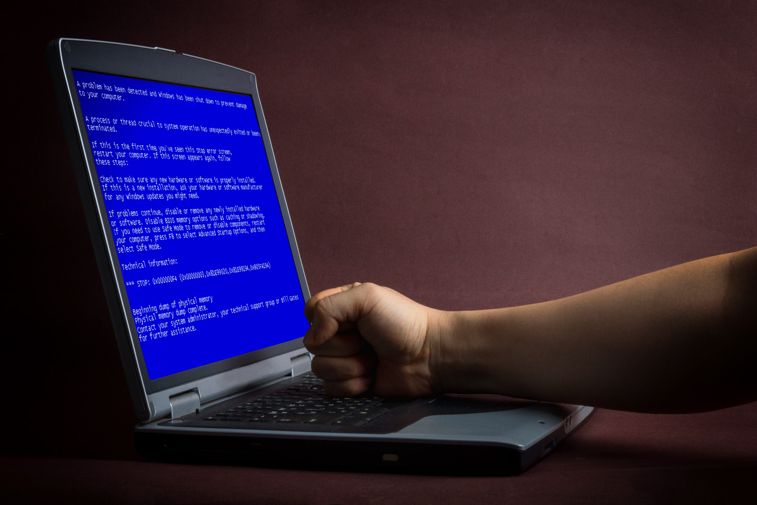 someone resting their fist on the keyboard of a blue laptop screen with coding on.