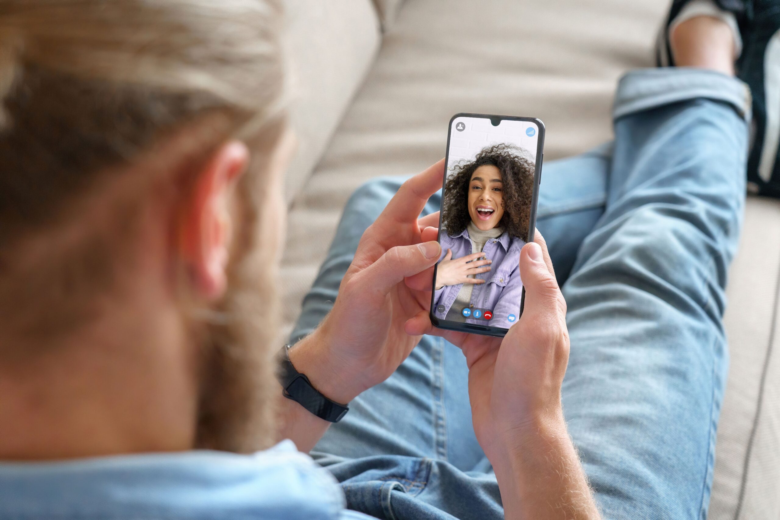 A man sitting on a couch using his android to video call a woman.