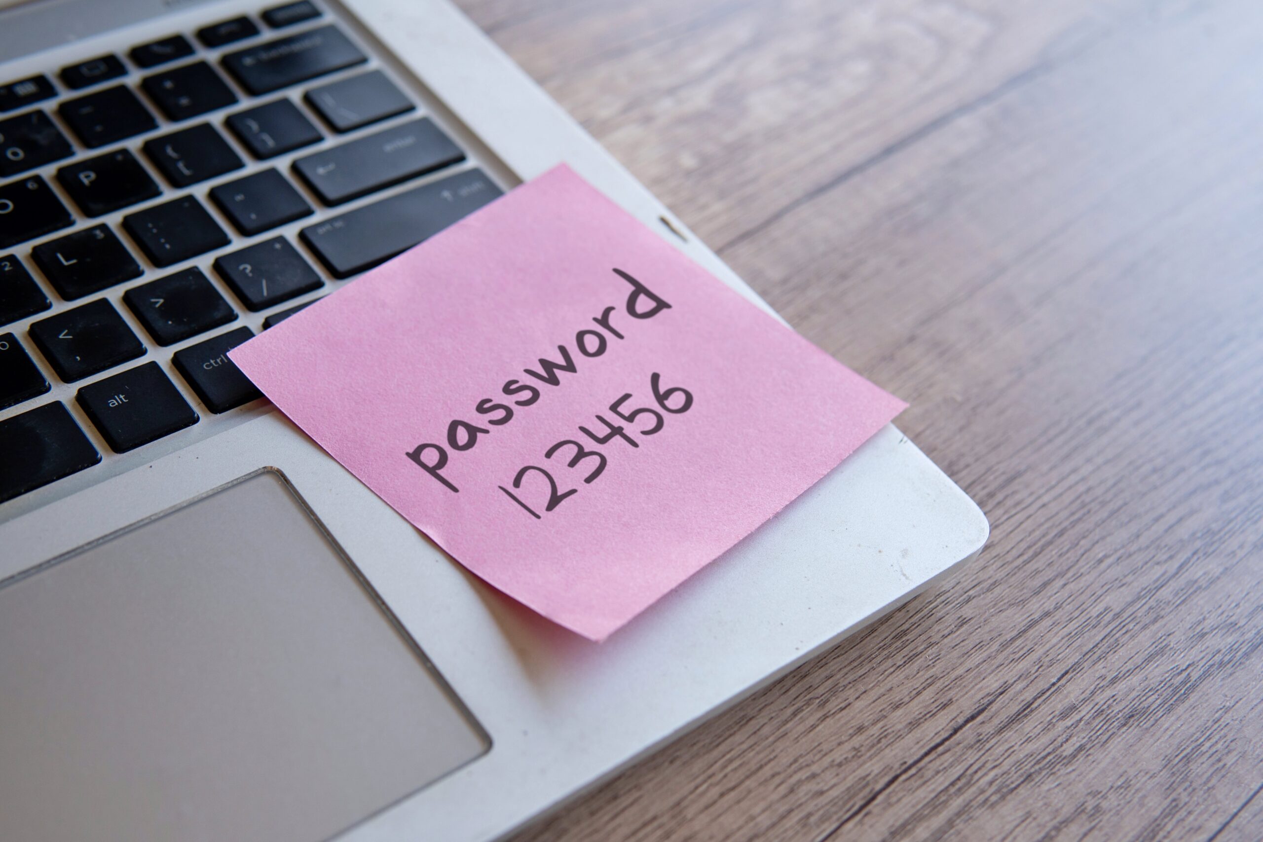 A pink sticky note placed on a laptop keyboard saying “Password 123456.”