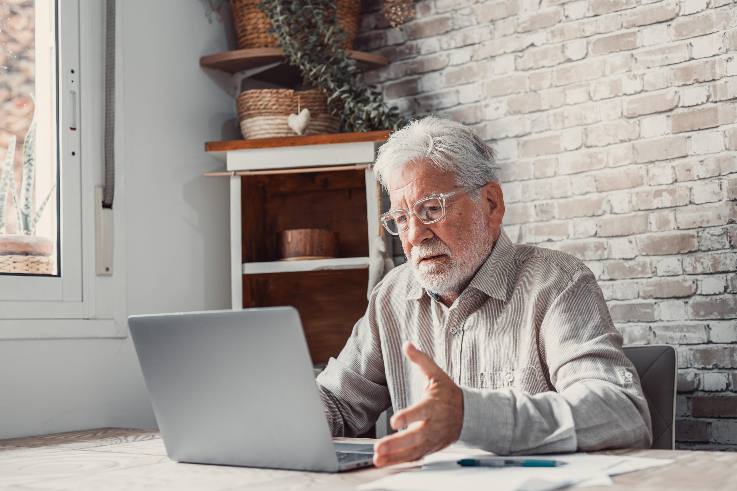 An elderly man sitting at his desk looking confused at what is being displayed on his computer screen.