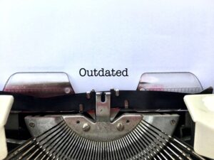 Close-up of a vintage typewriter typing the word “Outdated” on white paper, representing obsolete technology or systems.