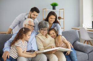 Happy multi-generational family sitting on a couch together, smiling and looking at a photo album