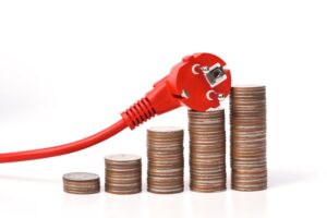 Red electrical plug resting on stacked coins, illustrating rising electricity costs or energy consumption associated with electronics.