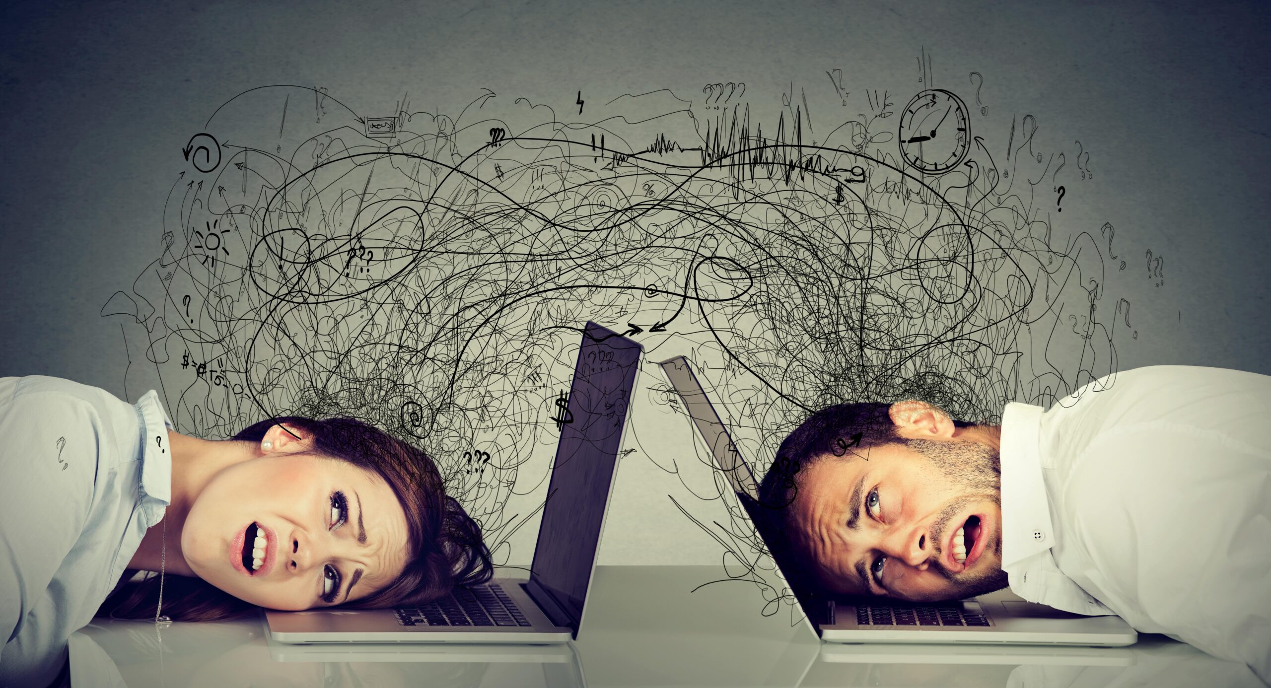 Stressed man and woman with their heads on laptops, surrounded by chaotic scribbles and symbols, representing tech overload or digital burnout.