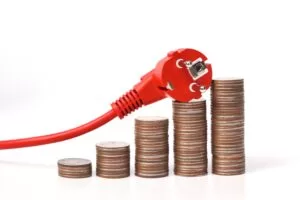 Red electrical plug resting on stacked coins, illustrating rising electricity costs or energy consumption associated with electronics.