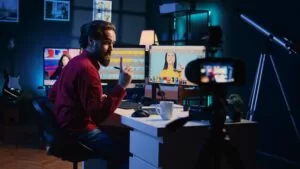 Man recording a video tutorial at his desk, editing photos on dual monitors, with a camera and lighting equipment set up in a modern studio. 
