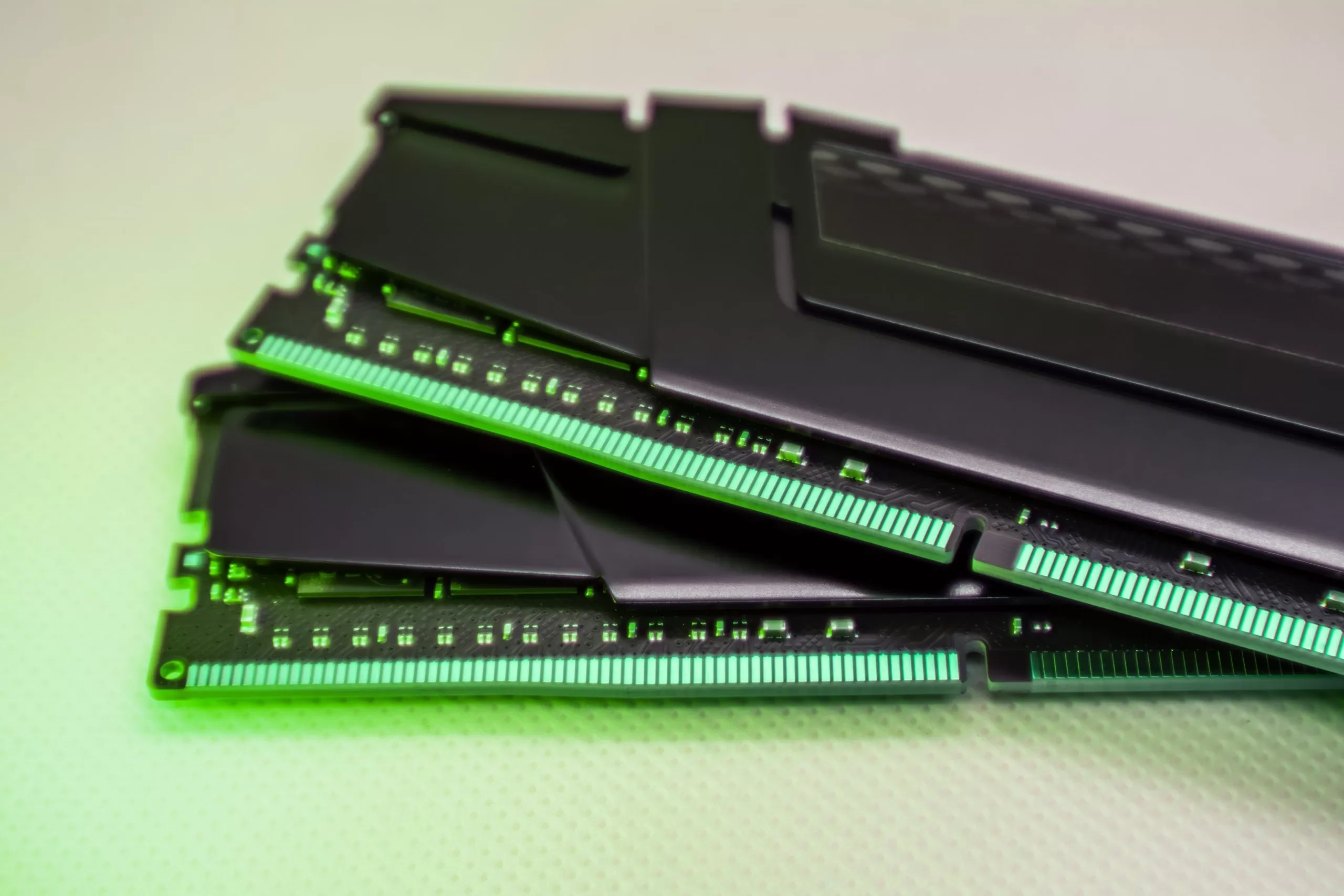 Close-up of stacked computer RAM modules with a black heat spreader and green circuit connectors, photographed under green-tinted lighting.